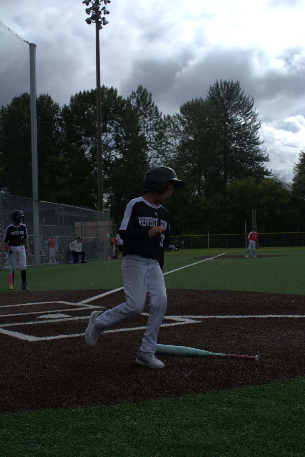 Young baseball player breaking out of the batter's box under a stormy sky